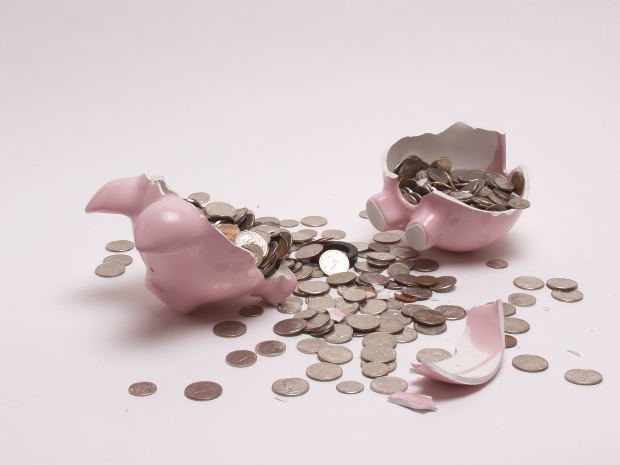 Broken piggy bank with coins spilling out around the peices