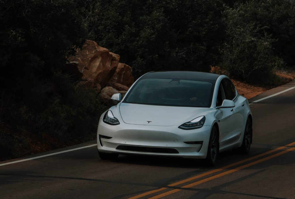 White tesla driving at dusk with no headlights on.