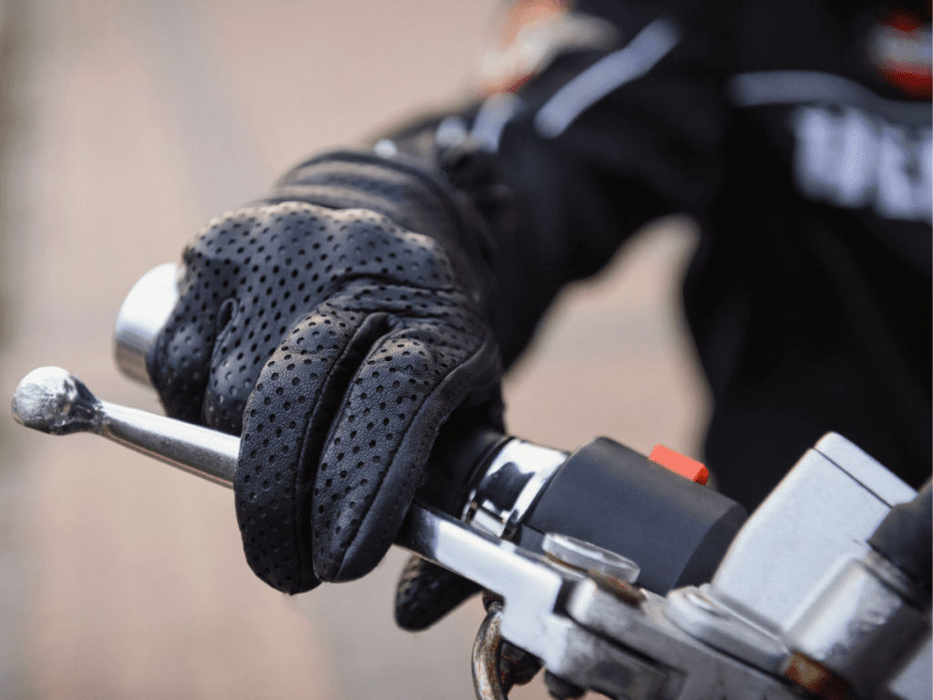 A gloved hand holding the throttle of a motorcycle.