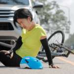 A woman on the ground next to her bike next to a car in the road.