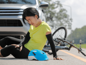 A woman on the ground next to her bike next to a car in the road.