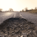 A close up of a pot hole in the middle of an asphalt road.