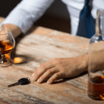 A mans hands on the top of a bar holding a drink and a car key.