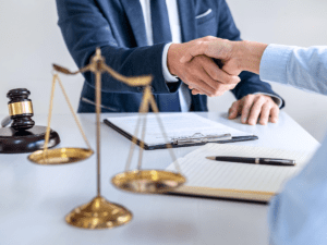 A handshake between two men over a table holding paper and a scale of justice.